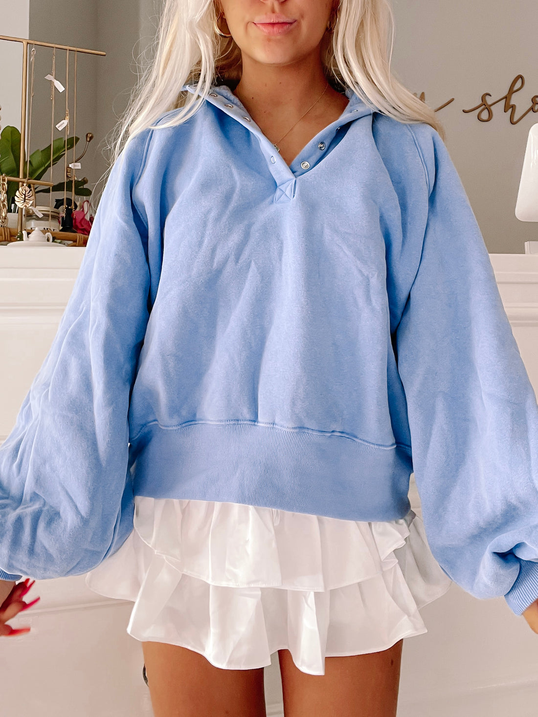 Light blue pullover sweatshirt with button detail, styled with a white ruffled skirt.
