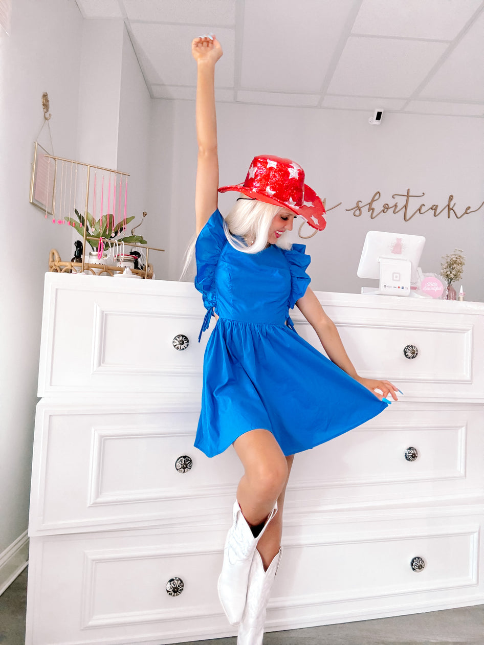 Bright blue mini dress with ruffle sleeves, modeled in a boutique setting.
