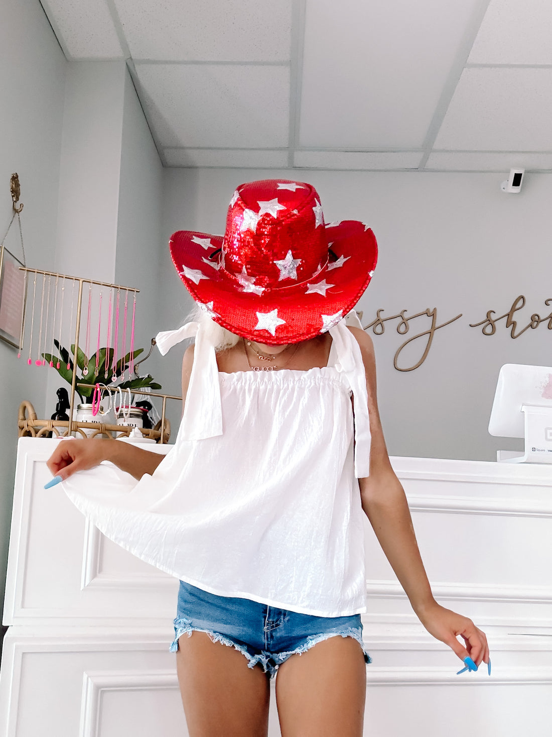 White ribbon top styled with denim shorts in a boutique setting.
