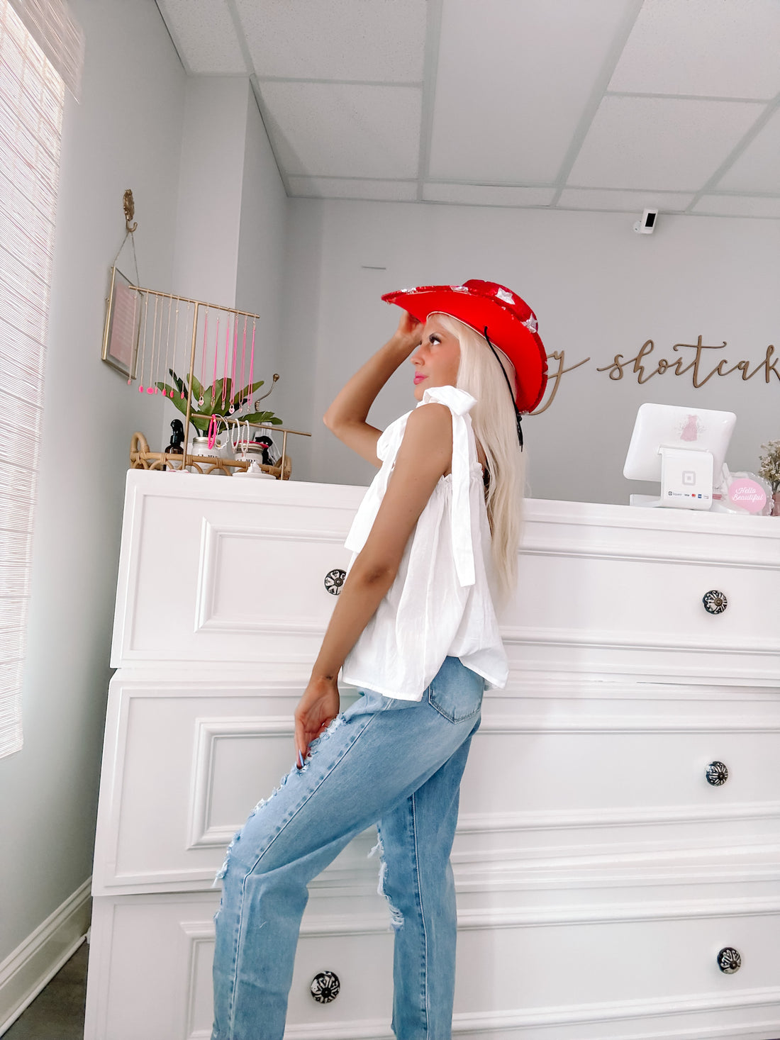 White eyelet ribbon top styled with light wash jeans, in a bright, airy shop setting.
