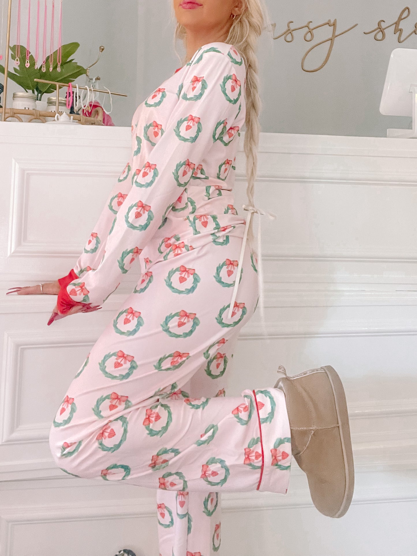 Pink pajama set with festive wreaths and bows, worn with tan slippers.

