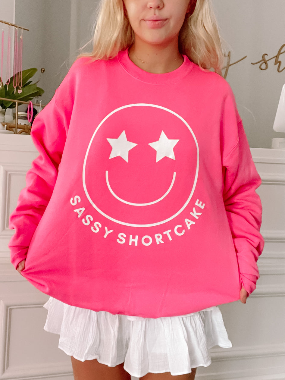 Hot pink crewneck sweatshirt featuring a smiling face graphic and "Sassy Shortcake" text.
