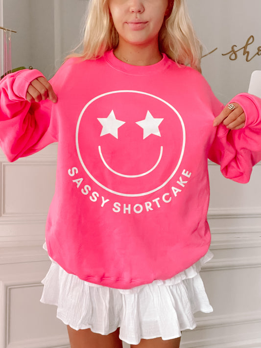 Hot pink crewneck sweatshirt featuring a smiling face graphic and "Sassy Shortcake" text.