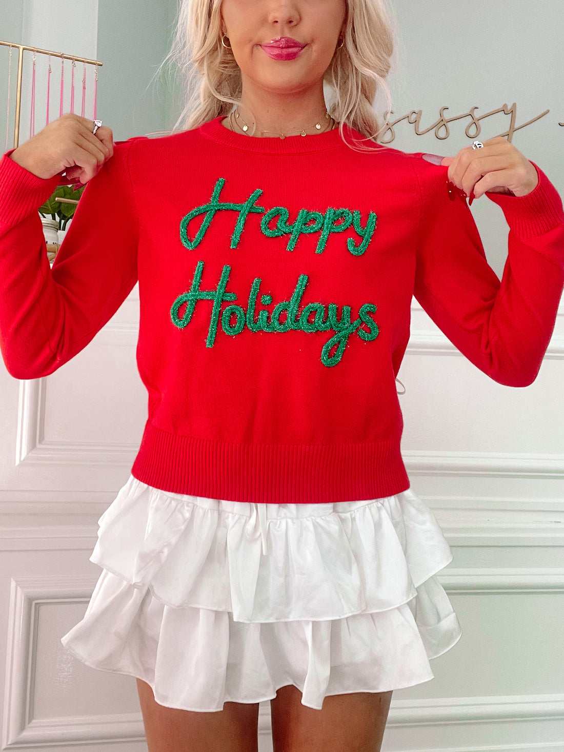 Red Christmas sweater with green sparkly "Happy Holidays" lettering, paired with a white ruffled skirt.
