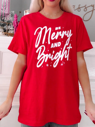 Person wearing a red t-shirt with 'Be Merry and Bright' text in a festive setting.