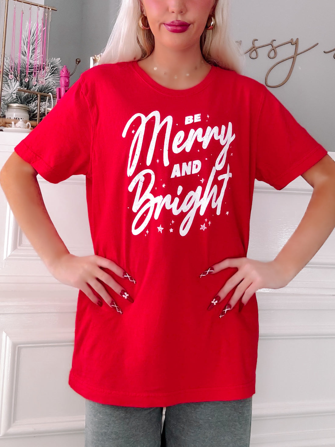 Person wearing a red t-shirt with 'Be Merry and Bright' text in a festive setting - Sassy Shortcake