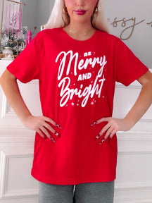 Person wearing a red t-shirt with 'Be Merry and Bright' text in a festive setting - Sassy Shortcake