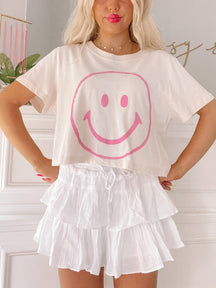 Cream cropped tee featuring a pink smiley face graphic.
