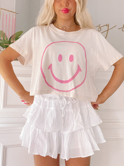Cream cropped tee featuring a pink smiley face graphic.
