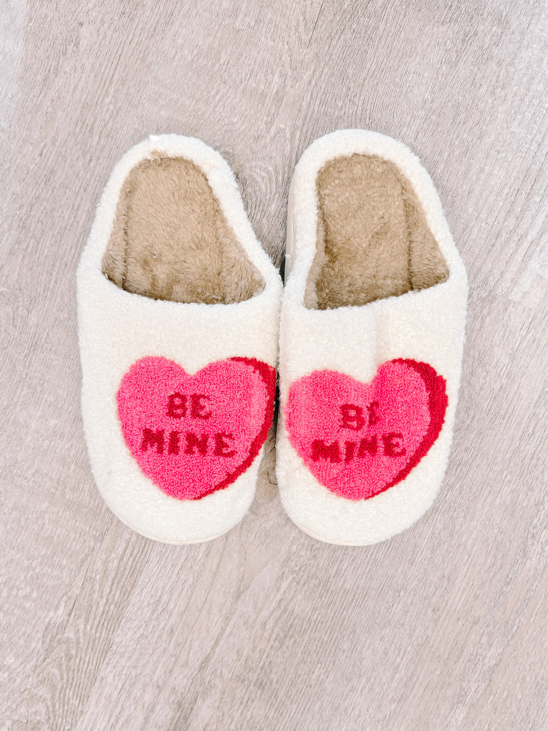 Cozy cream "Be Mine" heart slippers with pink heart details, perfect for Valentine's Day.
