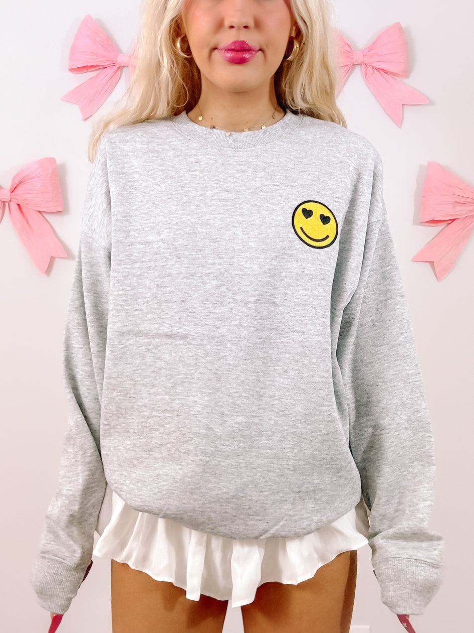 Grey Happy Heart crewneck sweatshirt with heart-eyed smiley face detail
