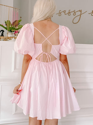 Pink mini dress with puff sleeves and an open back, shown on a model.
