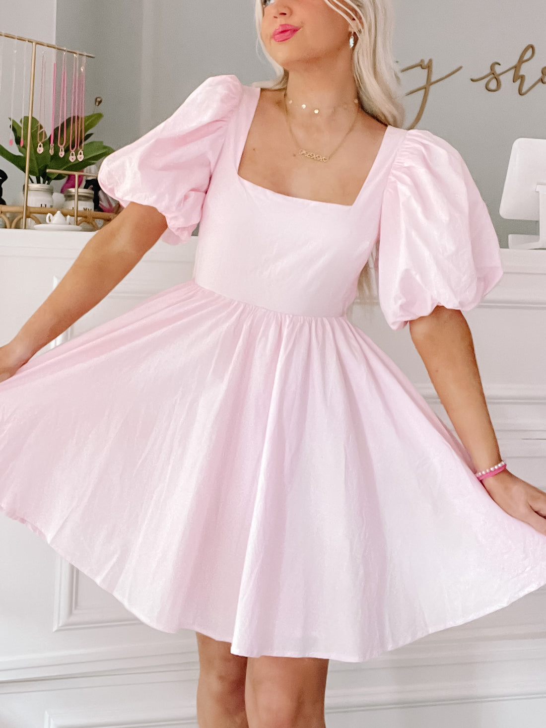 Pink puff-sleeve mini dress with a square neckline, shown on a model in a bright interior.
