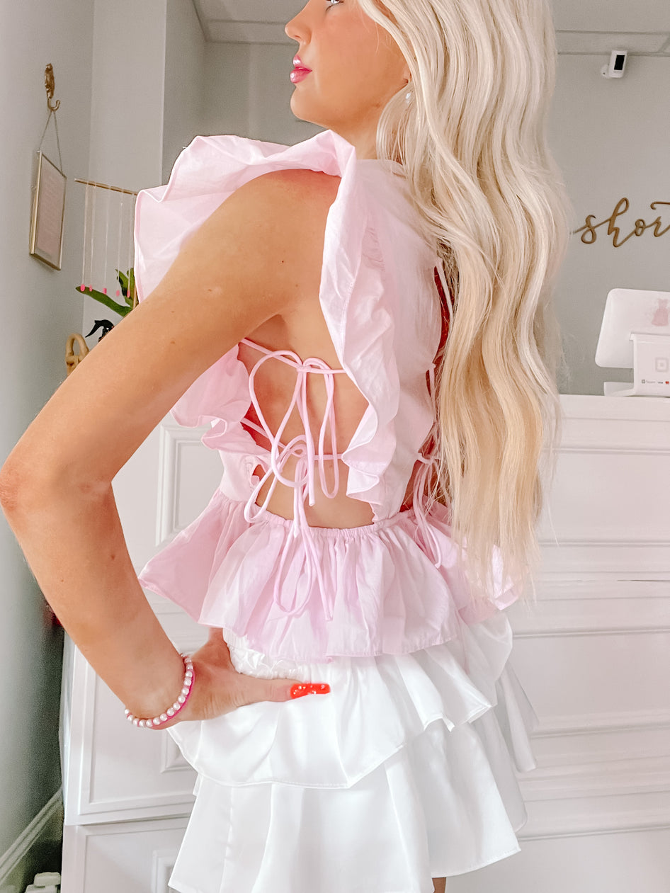 Pink ruffled crop top with open back, worn with a layered white skirt.
