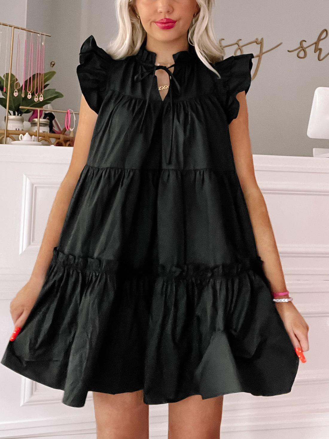 Black tiered mini dress with ruffle sleeves and a tie neckline, shown on a model.

