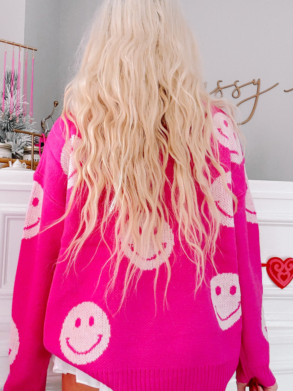 Pink knit sweater featuring a playful pattern of off-white smiley faces.
