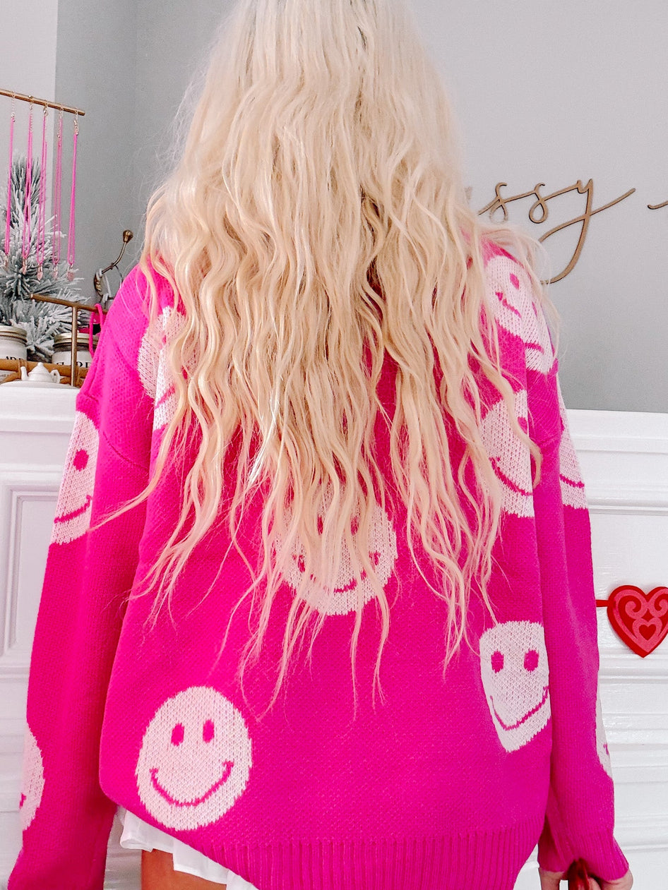 Hot pink knit sweater adorned with off-white smiley faces, shown from the back.
