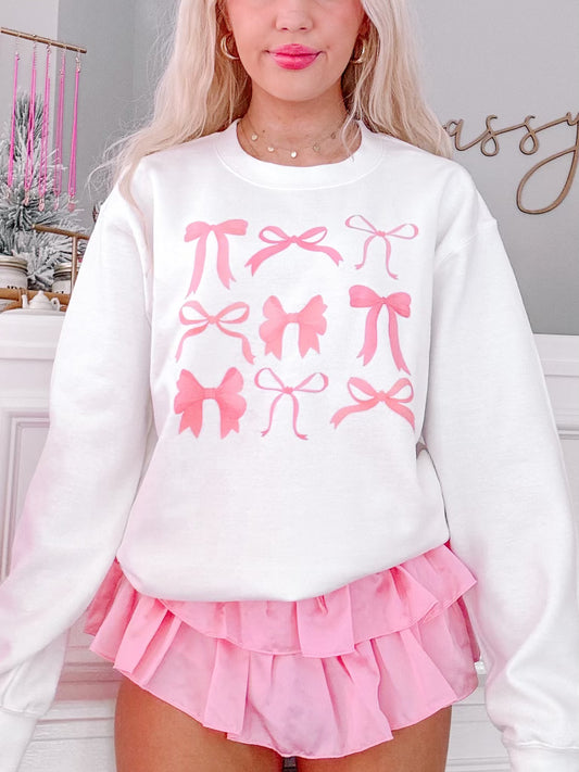 White crewneck sweatshirt featuring a pink bow print, modeled with a pink ruffled skirt.