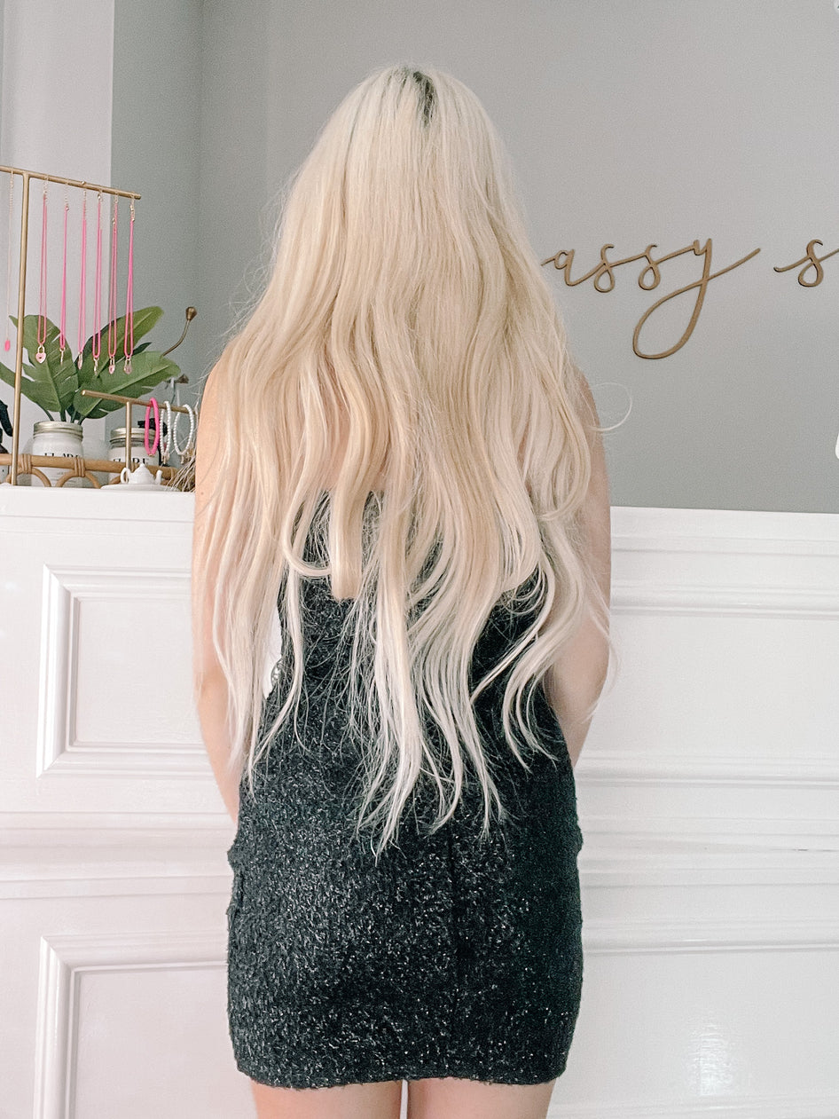 Sparkly black mini dress shown from the back, against a white wall.
