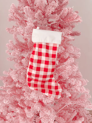 Red and white gingham Christmas stocking hanging on a pink flocked artificial tree.
