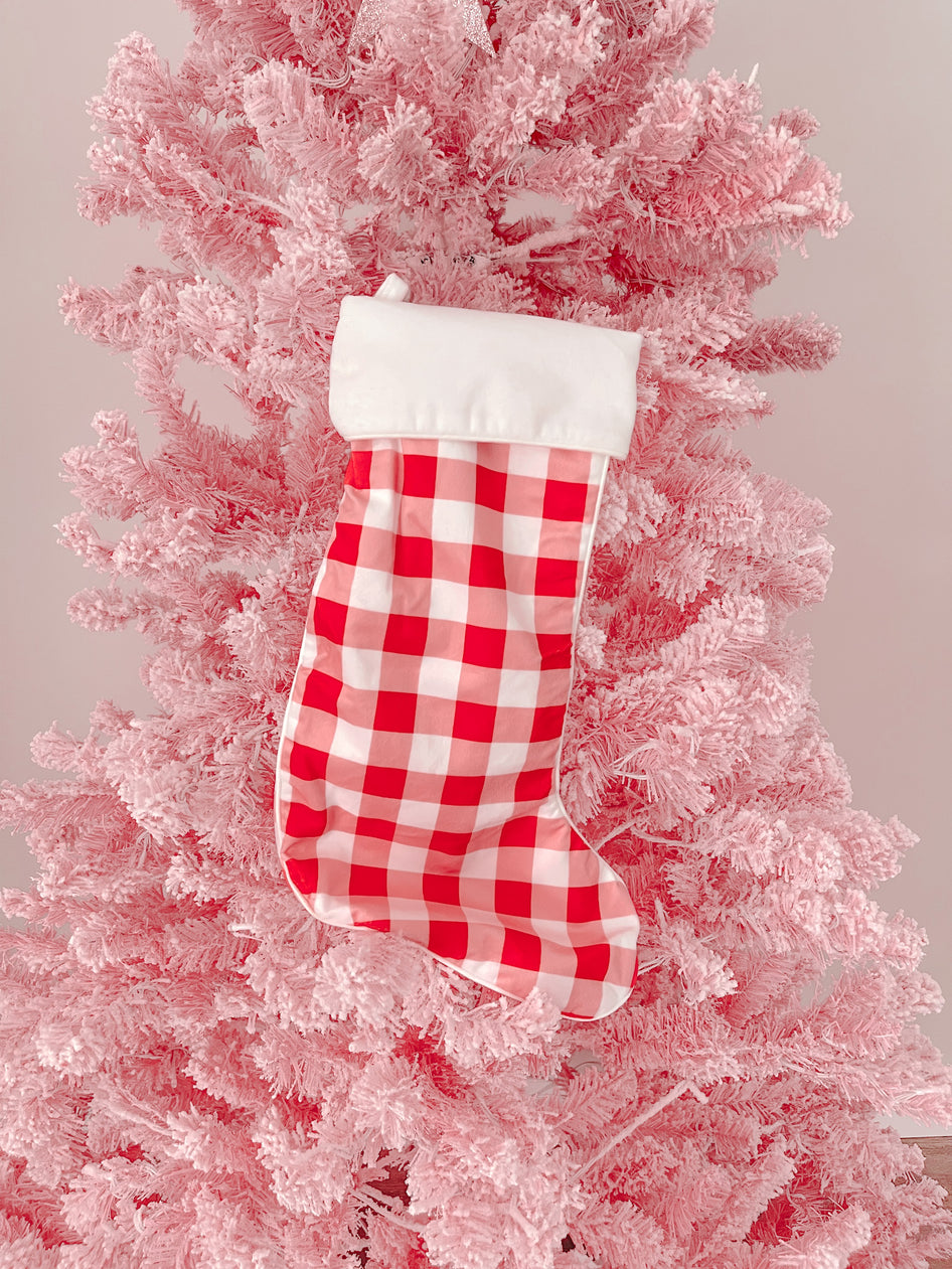 Red and white gingham Christmas stocking hanging on a pink flocked artificial tree.
