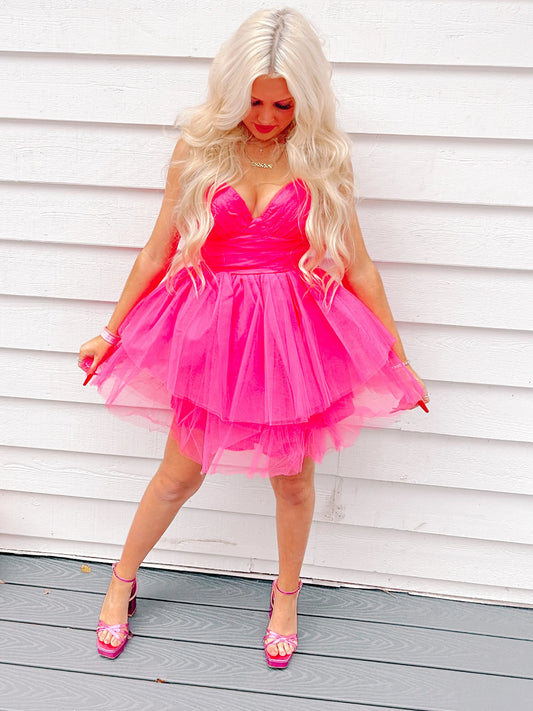 Hot pink tulle mini dress, layered skirt, worn against white wood siding.
