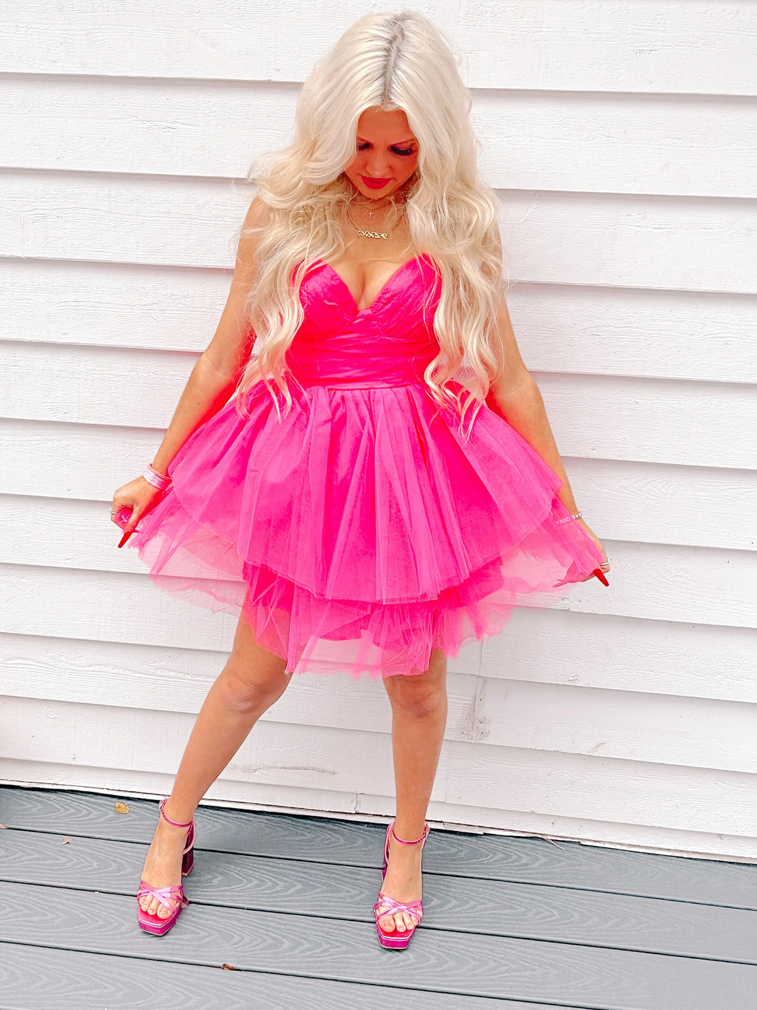 Hot pink tulle mini dress, layered skirt, worn against white wood siding.
