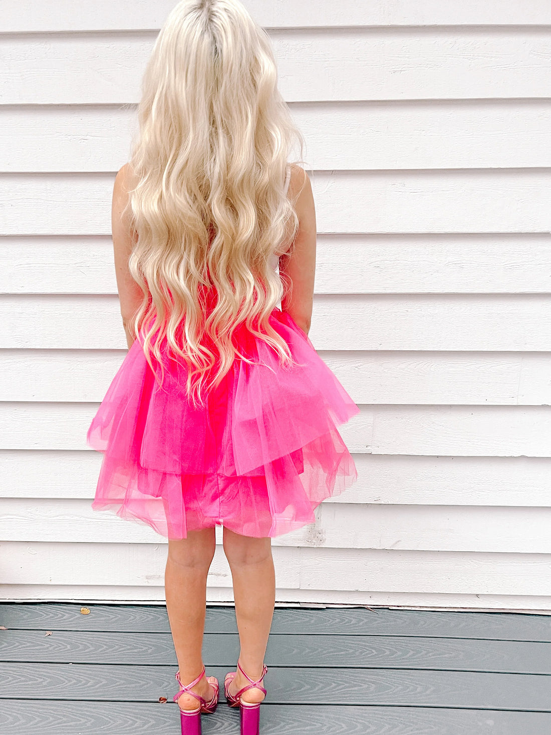 Hot pink tulle dress with layered skirt, shown from the back against a white wood backdrop.
