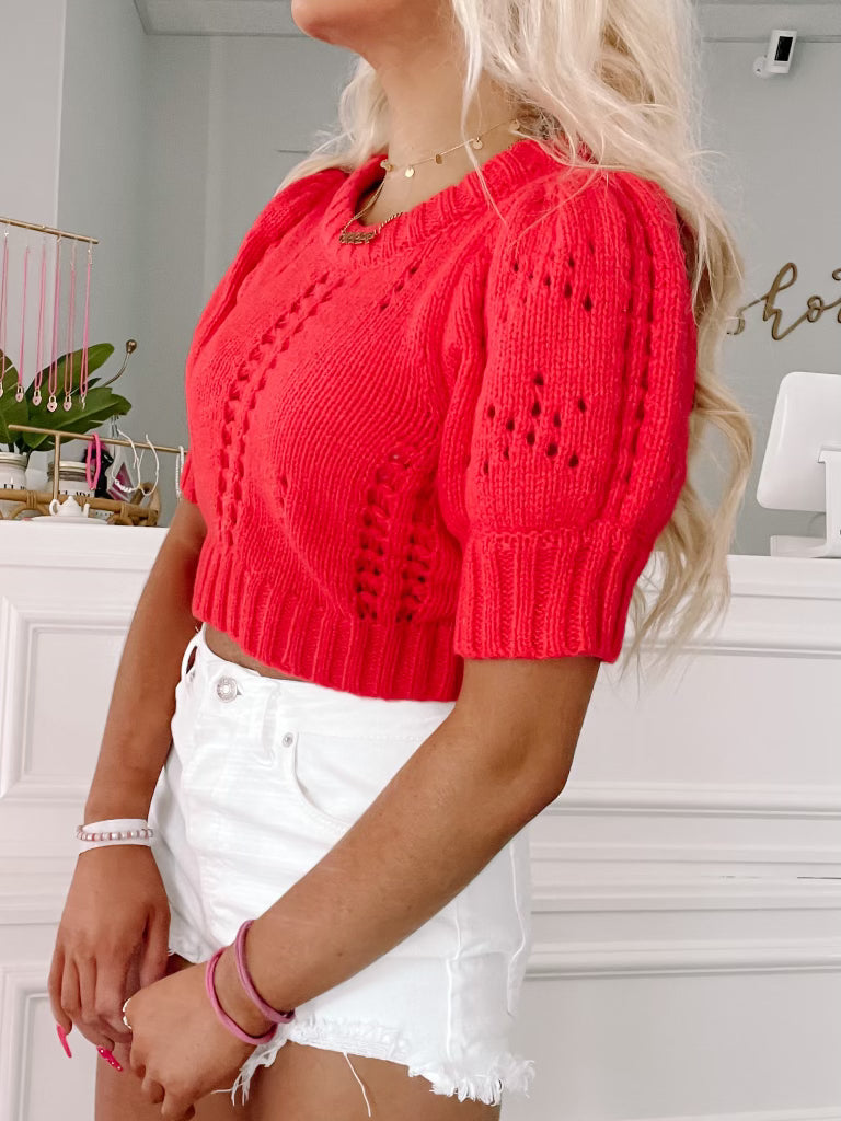 Red knit cropped sweater with puff sleeves, worn with white denim shorts.
