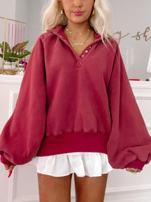 Burgundy oversized pullover sweater with balloon sleeves, styled with a white pleated mini skirt.
