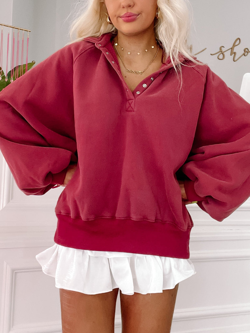 Burgundy pullover sweatshirt with balloon sleeves, styled with a white ruffled skirt.
