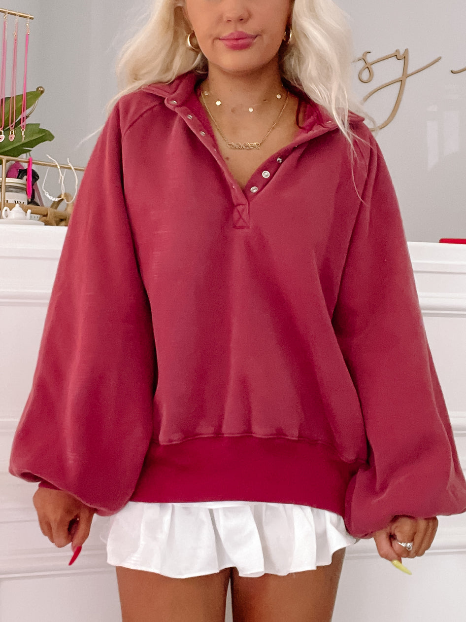 Burgundy pullover top with balloon sleeves, styled with a white pleated skirt.
