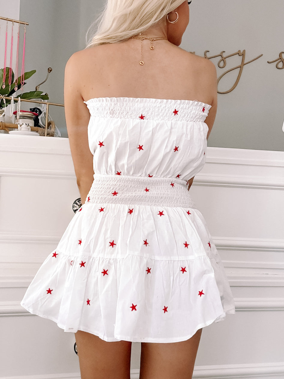 White mini dress with red star embroidery, viewed from the back.
