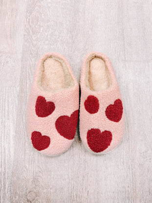 Pink fuzzy slippers with red heart accents for cozy comfort.
