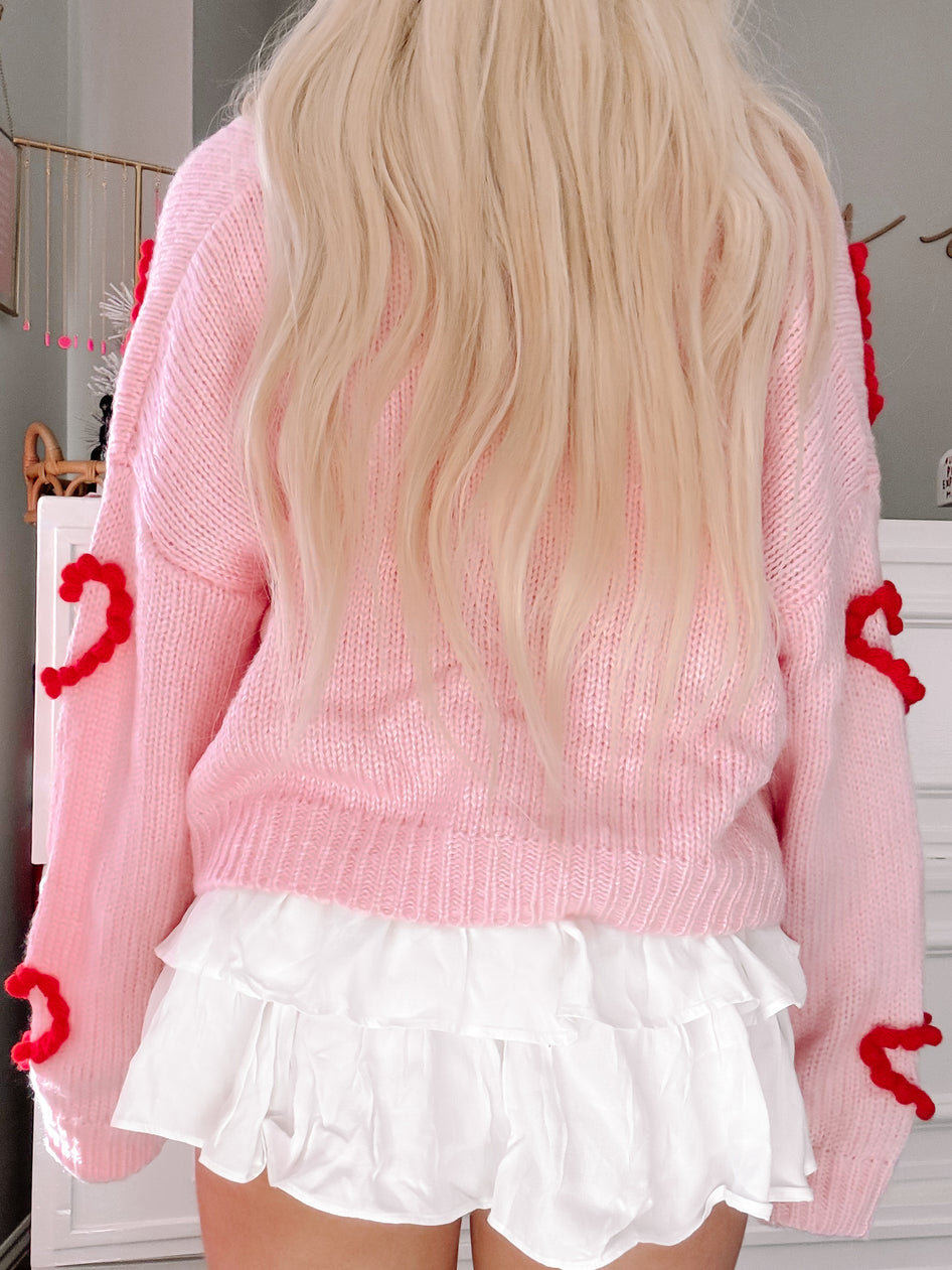 Pink knit cardigan with red heart detailing, shown from the back.

