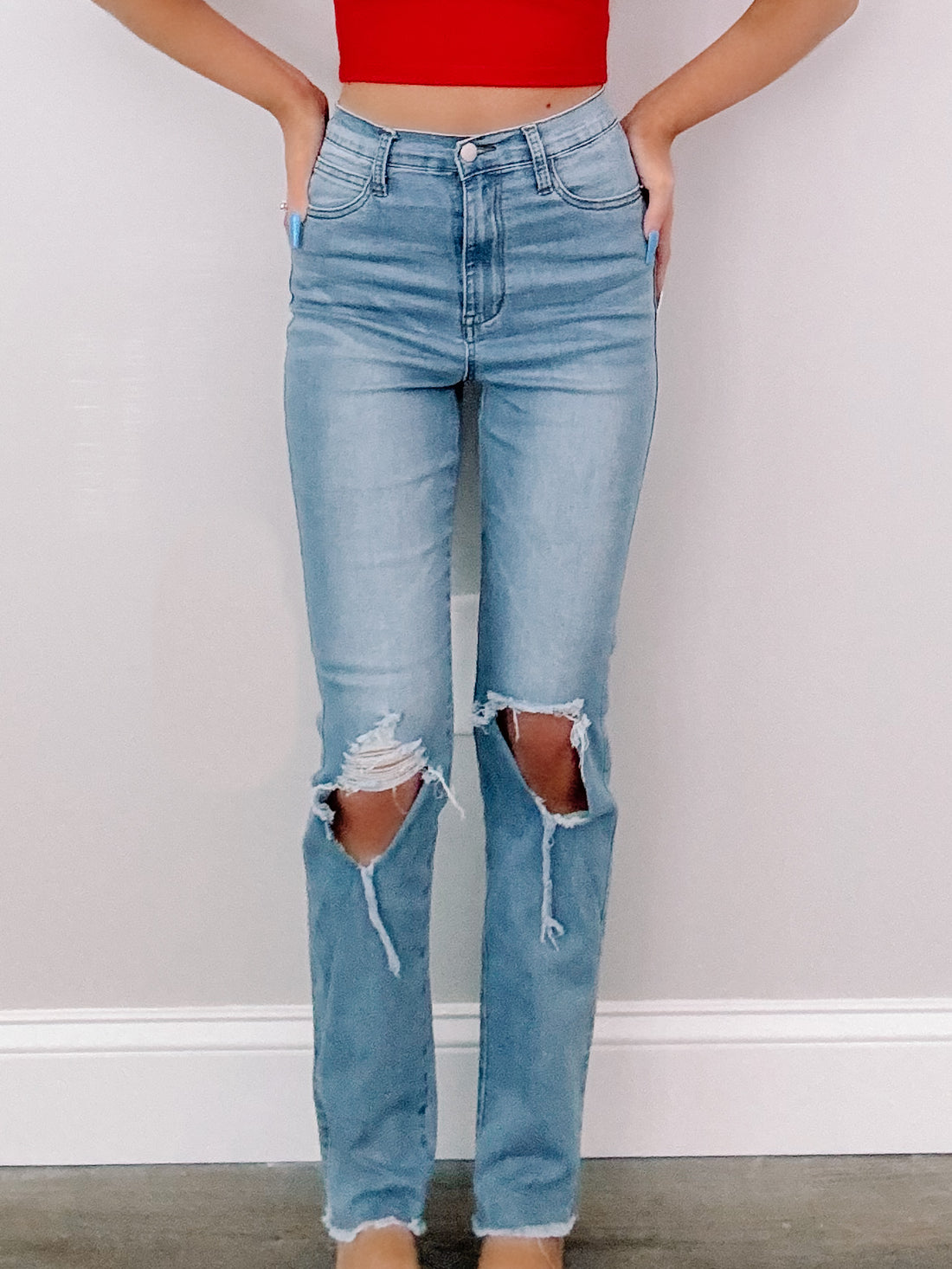 Light wash, distressed jeans with knee rips, shown against a neutral background.
