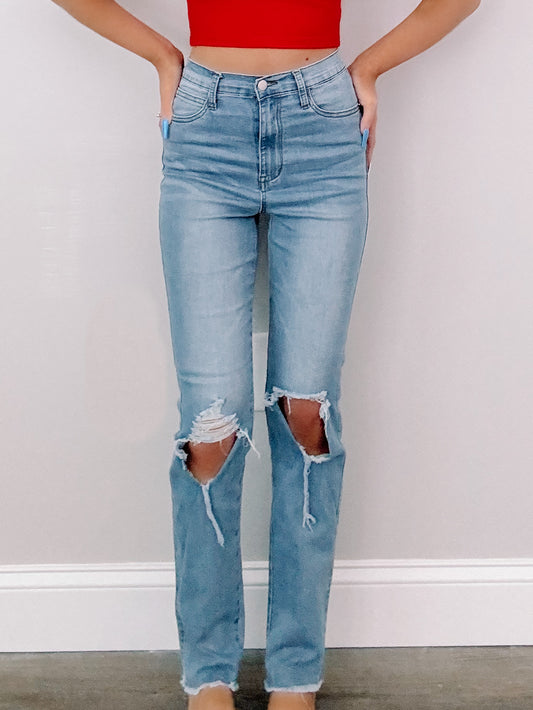 Light wash, distressed jeans with knee rips, shown against a neutral background.
