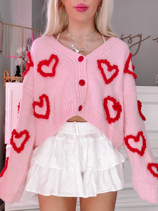 Pink cropped Love You Lots cardigan with red heart details; perfect for Valentine's Day.
