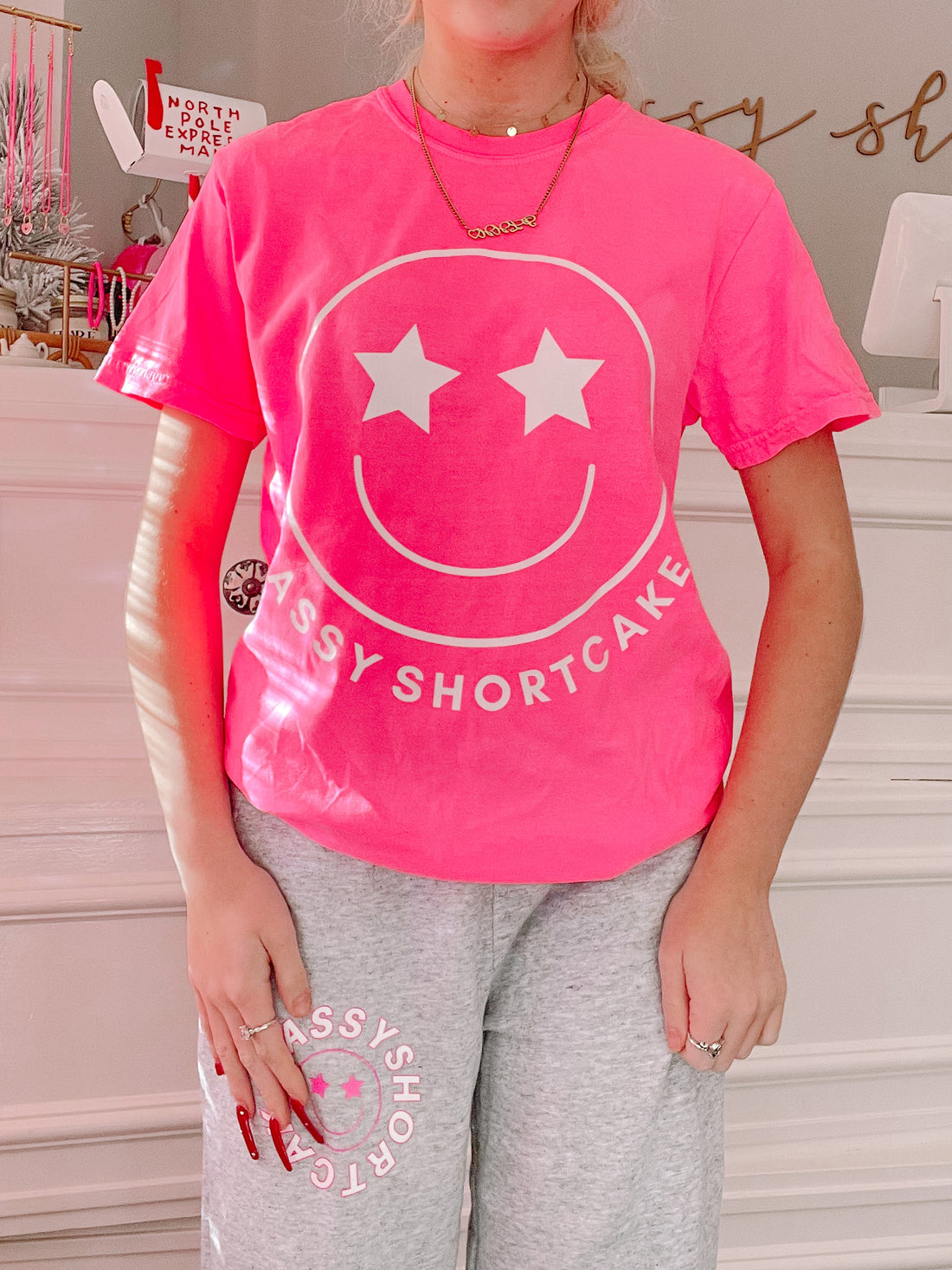 Bright pink short-sleeve tee featuring a smiling face graphic and "Sassy Shortcake" text.
