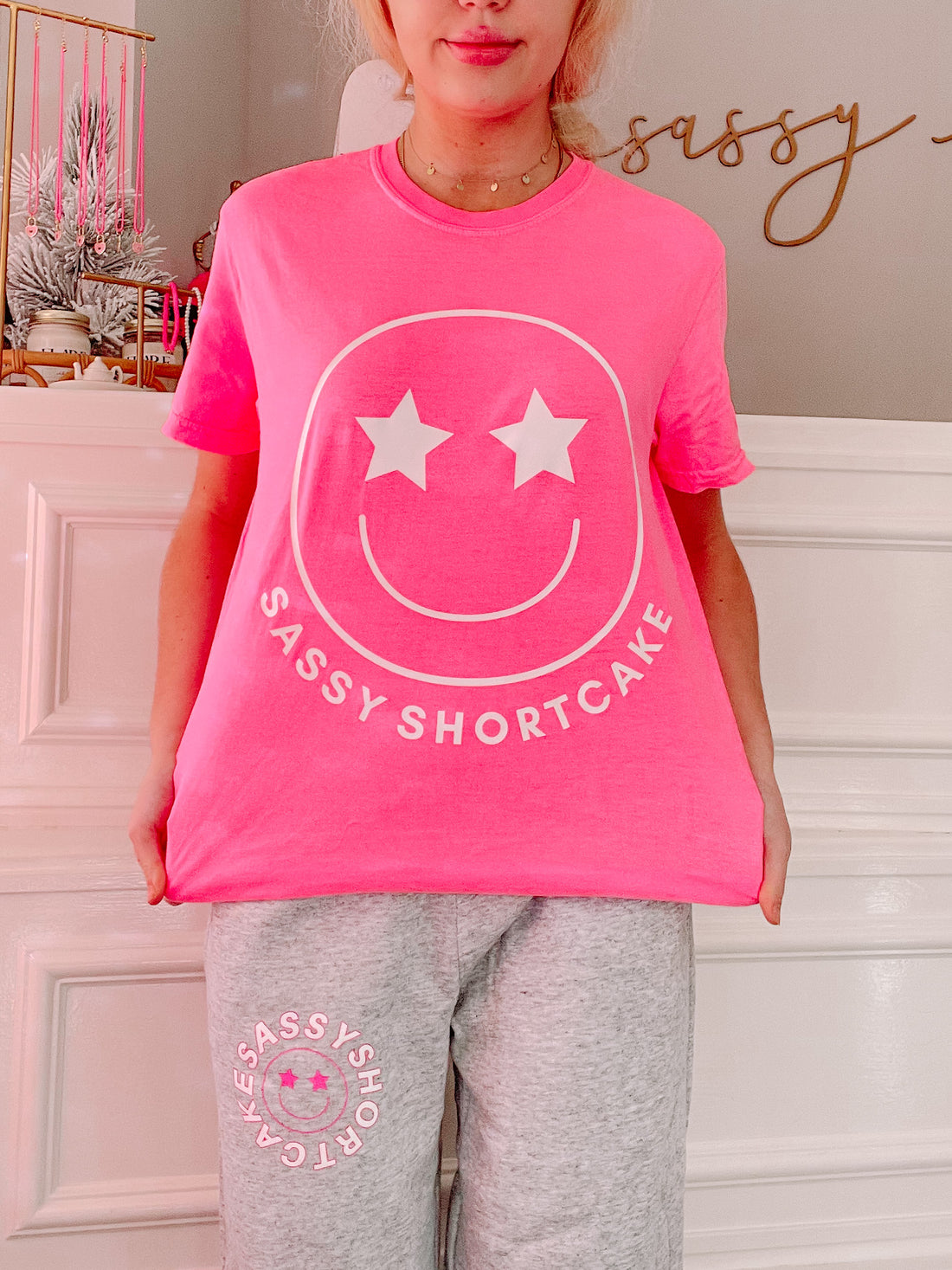 Bright pink t-shirt featuring a smiley face graphic and "Sassy Shortcake" text, shown on a model.
