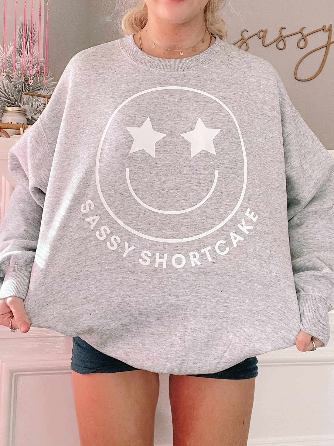 Grey crewneck sweatshirt featuring a smiling face graphic with star eyes.
