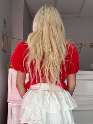 Red rose-embellished top paired with a white tiered skirt; seen from the back.
