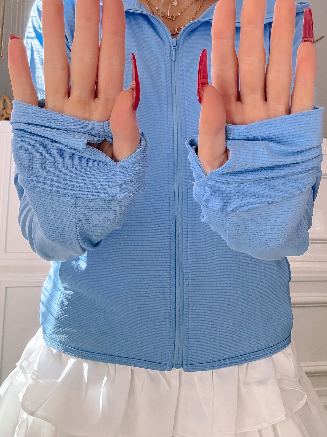 Light blue zip-up jacket with thumbholes, shown with a white skirt.
