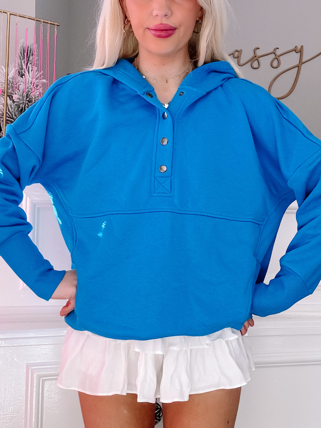 Bright blue hooded pullover with button placket, modeled over a white ruffle skirt.
