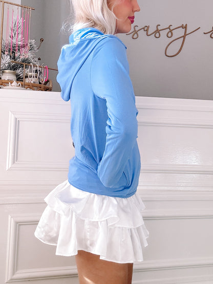 Light blue zip-up jacket with a white ruffled skirt, shown against a white wall.
