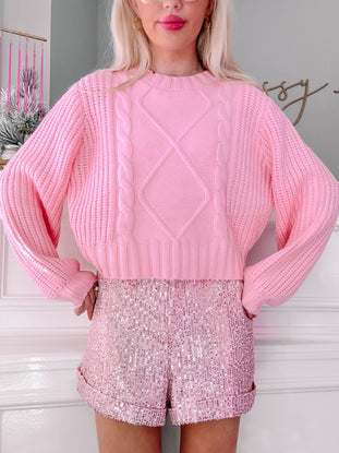 Pink sequin shorts paired with a pink cable knit sweater.
