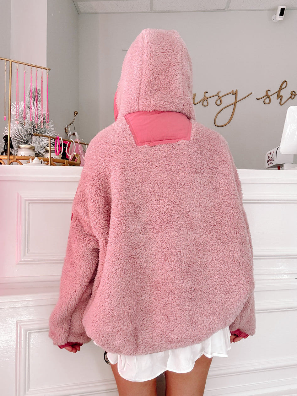 Pink sherpa pullover with a hood, shown from the back against a white wall.
