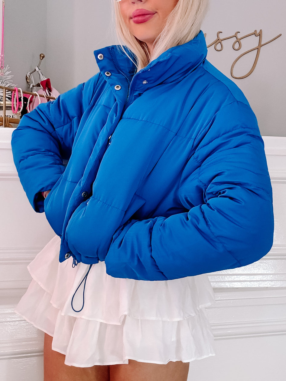 Bright blue puffer jacket styled with a white tiered skirt.
