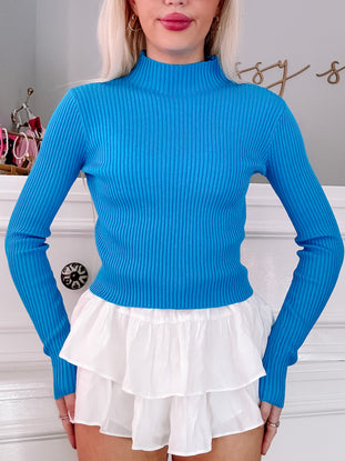 Bright blue ribbed knit mock neck top styled with white tiered shorts.
