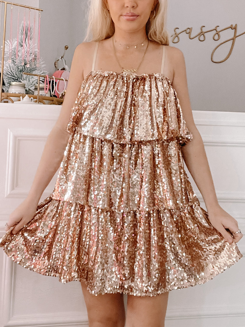Rose gold sequined mini dress with tiered ruffles, shown on a model against a neutral backdrop.
